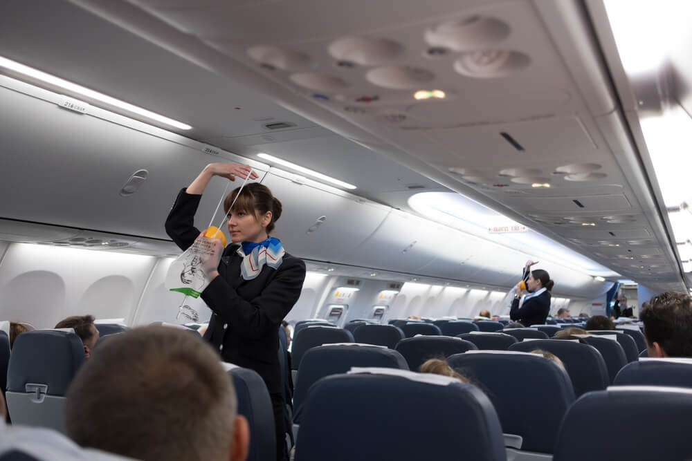 Flight attendant demonstrating safety procedures on an airplane, a topic recently covered in Afuzion news. | Afuzion