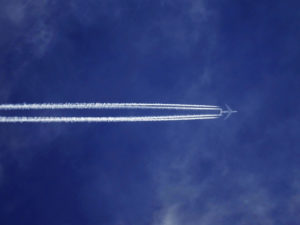 Airplane flying at high altitude, ensuring DO-254 compliance, leaving a condensation trail against a blue sky with wispy clouds. | Afuzion