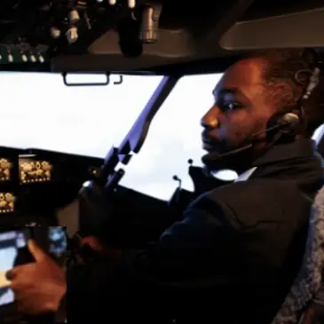 A man wearing a headset sits in an airplane cockpit, holding the controls and looking towards the camera—portraying the expertise found at AFuzion. | Afuzion